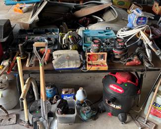 This table has shovels shot vacs multiple pumps, water pumps underneath the table on top of the table is a hammer drill, Milwaukee battery set with charger and batteries Ryobi corded saw and drill a magnum paint sprayer corded grinder shovels picks Brad nailer Dremel set other power tools stick sander a bucket of drywall screws about 1/3 full and two routers