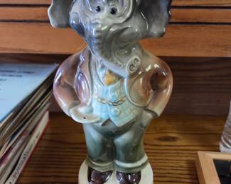 Charming ceramic decanter designed in the shape of a well-dressed elephant, complete with a cork stopper. Great as a whimsical barware piece, conversation starter, or collectible display item for lovers of vintage kitsch and animal-themed decor.