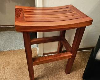 Teak wood shower bench with a curved slatted seat.