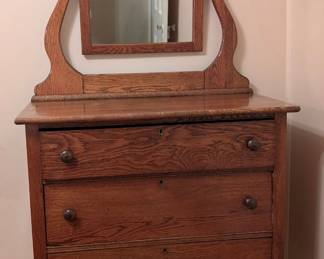 $100 Early 20th Century Chest of Drawers with Harp Mirror: Stained oak, the top with attached rectangular mirror on harp-shaped supports, the rectangular top above three long drawers.
Width: 34 in.; depth: 18 in.; height of cabinet: 35 in.; height overall: 66 ¼ in.; mirror plate: 19 ⅜ x 15 ⅜ in.
