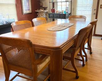Vintage, solid oak dining table with 6 wicker back rolling chairs.