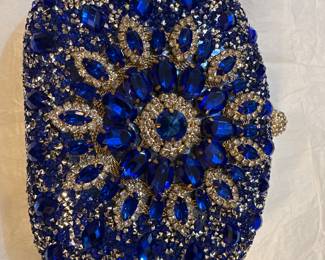 
This is a royal blue embellished clutch bag with gold details. 
