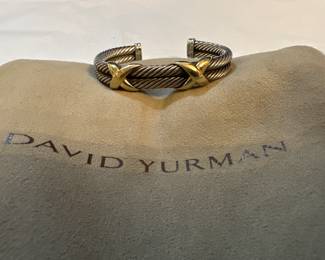 David Yurman 
The bracelet is a David Yurman two-tone double cable cuff bracelet. It is from the "X Collection" and features two twisted sterling silver cable bands with two 14-karat yellow gold "X" designs at the center. The original cable motif was inspired by the intertwining forms found in nature, as well as ancient and modern architecture