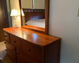 Large, solid wood dresser with matching framed mirror. Features seven  drawers with rounded wood knobs and smooth curved edges. A warm, polished finish complements the elegant silhouette.