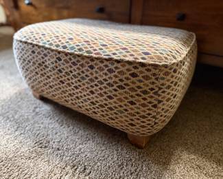 Low upholstered ottoman with a multicolor geometric pattern and wood feet.