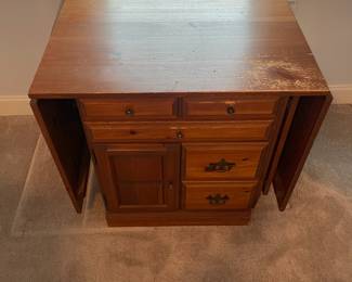 C6 - $50. Sewing Machine Table. Measures 33" wide x 24" deep x 28" tall. Each leaf adds 24". There is wear on the surface. Cabinet has 5 drawers, 1 door on hinges. (Needs minor work to reattach one leaf.)
