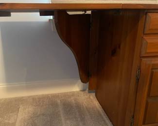 C6 - $50. Sewing Machine Table. Measures 33" wide x 24" deep x 28" tall. Each leaf adds 24". There is wear on the surface. Cabinet has 5 drawers, 1 door on hinges. (Needs minor work to reattach one leaf.)