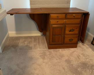 C6 - $50. Sewing Machine Table. Measures 33" wide x 24" deep x 28" tall. Each leaf adds 24". There is wear on the surface. Cabinet has 5 drawers, 1 door on hinges. (Needs minor work to reattach one leaf.)