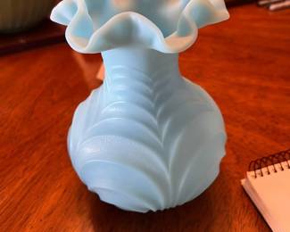 This is a vintage Fenton Blue Satin Glass Vase, featuring a ruffled rim and a drapery or leaf pattern. The vase was crafted sometime between the 1970s and 1980s. It is an example of art glass and may have a UV-reactive finish.
