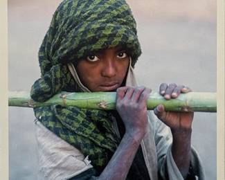 Jim Spillane (American, 1950s-) Photograph - "Ethiopia" | Portrait of a young woman wearing a green head scarf, carrying sugar cane across her shoulders. 
Photograph
Framed (gold frame) and matted (white)
Signed by artist (lower right): "Jim Spillane" in pencil
Titled by artist (lower center): "Ethiopia"
Numbered by artist: N/A
Sight: h. 9" x w. 9"