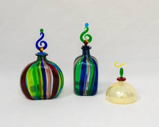 Two handblown Murano glass perfume bottles with multi-color stripes and glass stoppers, and a handblown art glass perfume bottle with a pale yellow ribbed base and a red, green, and yellow stopper. 