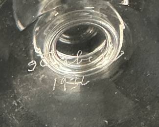 Closeup of two rare signed Steuben Glass works of art with hand-engraved designs by renowned sculptor and Steuben designer Sidney Waugh; the first a vase known as "Farm Laborers" vase, the male figure holding a pitchfork and the female figure holding a basket of produce; inscribed to base with Steuben and the date 1937. The second piece is a covered vase or urn with an Art Deco figure of a seated female nude playing a horn, inscribed on base with Steuben and the date 1936.