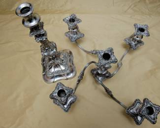 Another view of the exquisite antique silver plated five-light candelabra featuring four gracefully extending S-scroll arms adorned with applied stipple and chased leaf motifs, culminating in foliate repoussé drip pans and baluster-shaped candle cups with matching foliate-chased bobeches. The central candle cup mirrors this elaborate design, crowning the highly ornamented standard. The five-light section is removable, so that the baluster form base, richly embellished with foliate scrollwork, can be used as a single candlestick. There is a maker's mark to the underside of the five-light section, where it fits into the base.