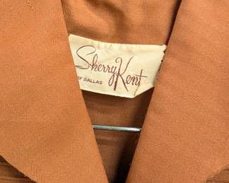 Closeup of a vintage terracotta color Sherry Kent of Dallas skirt suit with pin tucked short sleeve top, a straight skirt, and matching belt