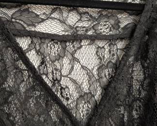 Closeup of H&M black lace blouse with short ruffled sleeves, button front closure and a black ribbon belt