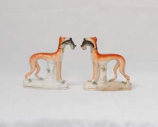 A rare matched pair of mid-Victorian Staffordshire pottery sighthounds (greyhound/whippet), modeled in mirror-image composition; each returning from the hunt with a hand-painted hare, set on a naturalistic base with tree-trunk support