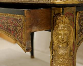 Closeup of the Napoleon III Boulle Inlay Bureau de Plat, 3rd quarter of the 19th Century. Crafted in the style of Louis XV with cabriole legs adorned with female allegorical figures, the red tortoiseshell top meticulously inlaid with brass depicting Diana the Huntress riding her chariot amidst scrolls and floral details. A large single drawer with a shield at center, and with a custom carved glass top.