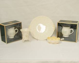 Two Belleek Ireland porcelain coffee mugs, one with the inscription "Whatever you do may the Luck of the Irish be with you!" and the other inscribed with "May your coffee be strong and your Monday be short," both in original boxes; a vintage Belleek porcelain tri-footed miniature spill vase with applied flowers and a basket weave pattern, a Belleek Ireland Tridacna pattern handled cake plate, and a Belleek porcelain shell design bon bon dish