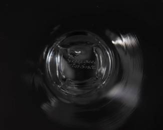 Closeup of one of the seven signed Lalique Phalsbourg pattern water goblets, 7 1/4 inches H. Each squared, frosted stem is molded with grape vines. Each sparkling glass is etched on the underside of the foot with Lalique France in script. Originally designed under Rene Lalique in 1924, this pattern was made 1924 - 2021.