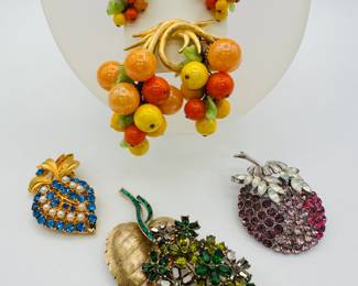 A fabulous fruit salad demi-parure featuring clip earrings and brooch; a large signed Crown Trifari floral spray brooch of heart-shaped gold tone metal leaf with stem of blossoms in a range of green faceted glass stones; a Faux Pearl and blue rhinestone brooch strawberry shaped brooch; and a signed Coro Pegasus berry brooch in rich pink and ruby color rhinestones in silver tone setting with pale navette stones at the top
