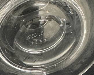 Closeup of two rare signed Steuben Glass works of art with hand-engraved designs by renowned sculptor and Steuben designer Sidney Waugh; the first a vase known as "Farm Laborers" vase, the male figure holding a pitchfork and the female figure holding a basket of produce; inscribed to base with Steuben and the date 1937. The second piece is a covered vase or urn with an Art Deco figure of a seated female nude playing a horn, inscribed on base with Steuben and the date 1936.