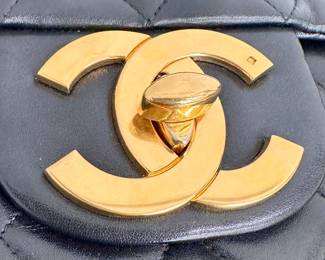 A closeup of the vintage Chanel Classic Flap Bag, black quilted lambskin leather with gold-tone hardware—an interlocking CC turnlock clasp—and a chain strap laced with leather. Authenticated by Entropy.