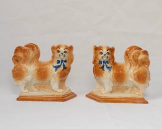 An antique pair of Bo’ness Scotland ceramic Pekinese dog figurines, made in mirror image, and wearing blue bows at the collar