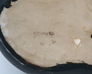 Closeup of the base of the charmingly dramatic ceramic sculpture of a black cat with a gold collar, signed by artist on the base