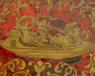 Closeup of the Napoleon III Boulle Inlay Bureau de Plat, 3rd quarter of the 19th Century. Crafted in the style of Louis XV with cabriole legs adorned with female allegorical figures, the red tortoiseshell top meticulously inlaid with brass depicting Diana the Huntress riding her chariot amidst scrolls and floral details. A large single drawer with a shield at center, and with a custom carved glass top.