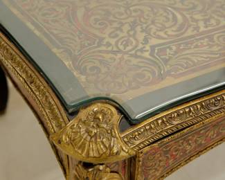 Closeup of the Napoleon III Boulle Inlay Bureau de Plat, 3rd quarter of the 19th Century. Crafted in the style of Louis XV with cabriole legs adorned with female allegorical figures, the red tortoiseshell top meticulously inlaid with brass depicting Diana the Huntress riding her chariot amidst scrolls and floral details. A large single drawer with a shield at center, and with a custom carved glass top.