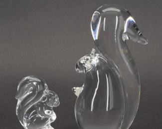 Two signed Steuben Glass squirrels - figurine and hand cooler. The large squirrel figurine designed for Steuben by George Thompson in 1974 features a whimsical form with a long bushy tail and delicate, perked ears. The second squirrel’s compact and evocative form is from Steuben’s “hand cooler" series, a cooling work of art to fit in the palm of your hand.
