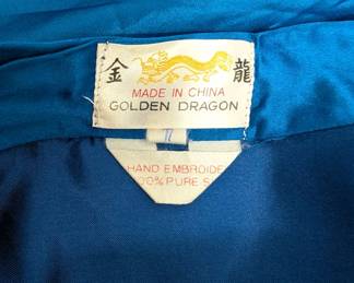 Closeup of the vintage Chinese blue silk robe, hand-embroidered front and back with multicolor flowers, trees, pagodas and pavilions; Golden Dragon label.