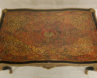 Another view of the Napoleon III Boulle Inlay Bureau de Plat, 3rd quarter of the 19th Century. Crafted in the style of Louis XV with cabriole legs adorned with female allegorical figures, the red tortoiseshell top meticulously inlaid with brass depicting Diana the Huntress riding her chariot amidst scrolls and floral details. A large single drawer with a shield at center, and with a custom carved glass top.