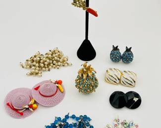 The charm of colorful vintage costume jewelry... Danecraft carrot brooch with matching dangle earrings, a pineapple brooch in gold-tone metal with turquoise color beads, pair of Austrian crystal pineapple earrings, black circular faceted clip on earrings, made in West Germany; pink straw hat clip on earrings, made in Western Germany; pair of Crown Triffari Faux Pearl cluster earrings, clip fittings; pair of gold tone and white enamel clip earrings; a pair of sterling silver, rhinestone, and blue glass bead earrings; and a pair of BSK clip earrings, silver tone metal with white enamel leaf shapes and jewel cut glass pieces in pink, ice blue, and spring green
