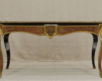 Another view of the Napoleon III Boulle Inlay Bureau de Plat, 3rd quarter of the 19th Century. Crafted in the style of Louis XV with cabriole legs adorned with female allegorical figures, the red tortoiseshell top meticulously inlaid with brass depicting Diana the Huntress riding her chariot amidst scrolls and floral details. A large single drawer with a shield at center, and with a custom carved glass top.