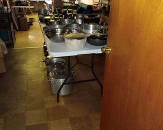 Pots and pans, with camping and hunting material in the back ground. In picture in the back are rooster and other figurines.