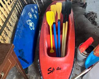 A kayak with paddles and a surfboard on the left.