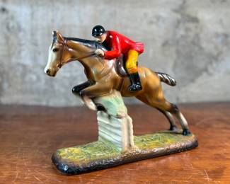 This lot features a sculpture of a jockey on a horse jumping over a fence, manufactured by ABCO, otherwise known as the Alexander Backer Company. In good overall condition with minor wear shown in photos, original ABCO sticker underneath, and measures, 9” H x 11” W x 3.5” D.
