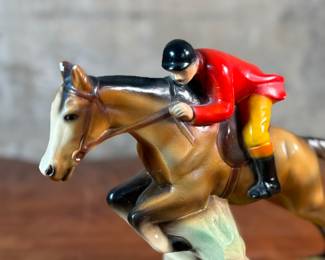 This lot features a sculpture of a jockey on a horse jumping over a fence, manufactured by ABCO, otherwise known as the Alexander Backer Company. In good overall condition with minor wear shown in photos, original ABCO sticker underneath, and measures, 9” H x 11” W x 3.5” D.
