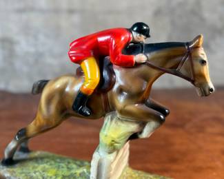 This lot features a sculpture of a jockey on a horse jumping over a fence, manufactured by ABCO, otherwise known as the Alexander Backer Company. In good overall condition with minor wear shown in photos, original ABCO sticker underneath, and measures, 9” H x 11” W x 3.5” D.
