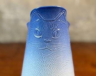 This lot features a Tschudy pottery cat vase pitcher in excellent overall condition, with maker mark underneath, and measures, 8” H x 5” W x 6” D. This ceramic vase has a cat face design with a blue and white ombre glaze.
