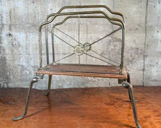 This lot features an Art Nouveau brass and wood magazine rack circa 1930s that measures, 18.5” H x 20.5” W x 12.5” D.
