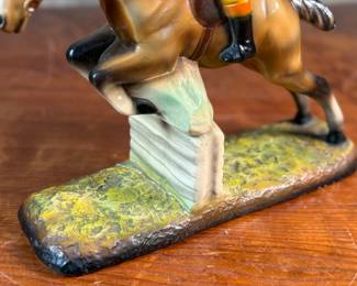 This lot features a sculpture of a jockey on a horse jumping over a fence, manufactured by ABCO, otherwise known as the Alexander Backer Company. In good overall condition with minor wear shown in photos, original ABCO sticker underneath, and measures, 9” H x 11” W x 3.5” D.
