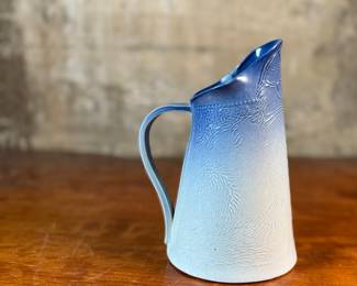 This lot features a Tschudy pottery cat vase pitcher in excellent overall condition, with maker mark underneath, and measures, 8” H x 5” W x 6” D. This ceramic vase has a cat face design with a blue and white ombre glaze.

