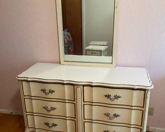 Six-drawer dresser with attached mirror in cream and gold finish. Curved front design with ornate drawer pulls. Some wear to painted surfaces. Approx. 18" x 49.5" x 32"