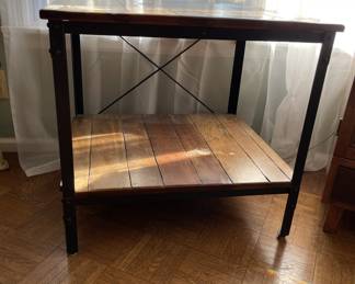 Matching wood and metal end table featuring a sturdy plank top, lower storage shelf, and black metal frame with crossbar support. See photo of spot on lower storage shelf. Approx. 26"x 23" x 24". Complements the industrial coffee table (Lot #1131).