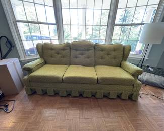 This is a three-cushion, vintage MCM Flexsteel sofa upholstered in a textured green fabric, featuring a tufted backrest, rolled arms, and a decorative ruffled skirt along the base. One leg has been replaced in the back, hidden by skirt. Approx 82" x 35" x 32"