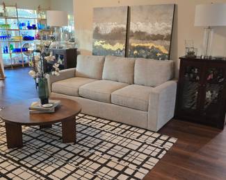 Neutral sofa, area rug, round coffee table, 2 curios full of interesting collectibles, and a pair of glass lamps