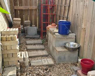 various garden supplies - bricks, stones, planters, trellises, stakes