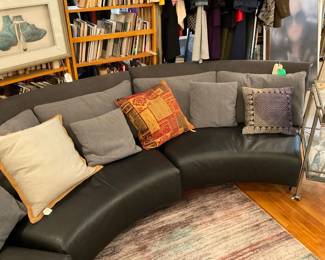Curved, contemporary leather sectional couch with grey cloth pillows.